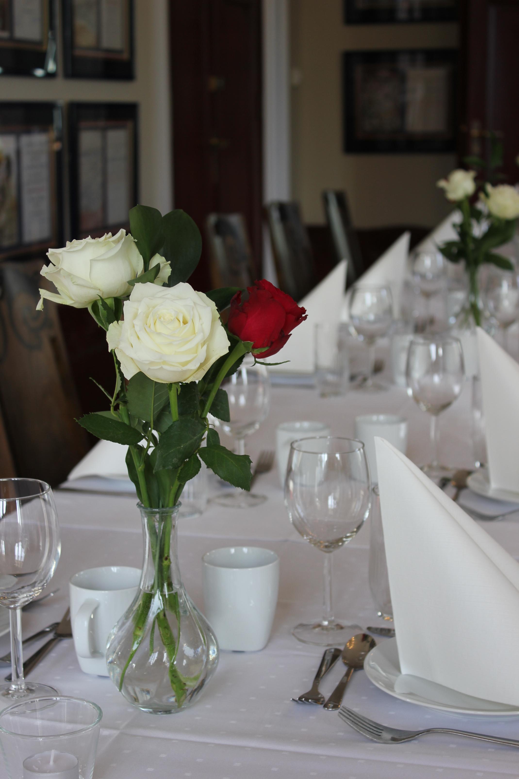 Nærbilde av pyntet bord med hvite og røde roser i vase og servise på hvit duk.